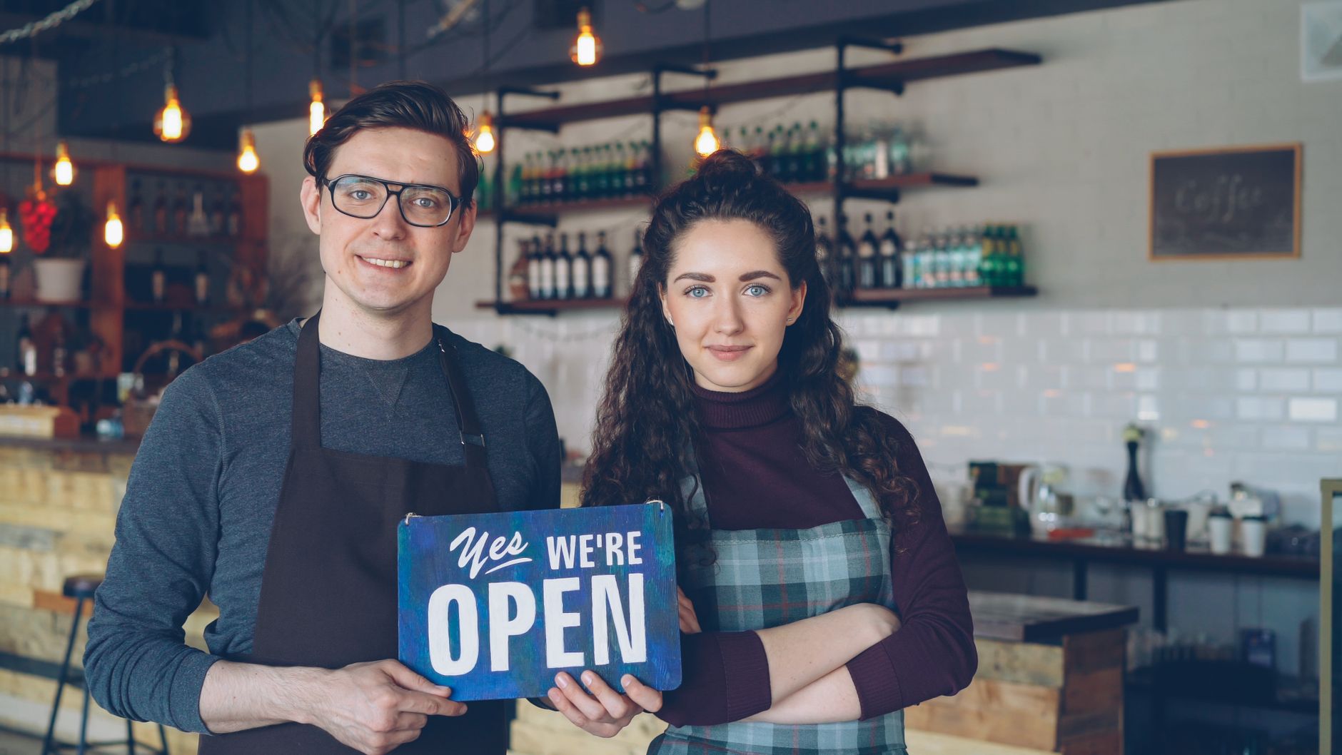 Two small business owners holding an Open sign in their shop